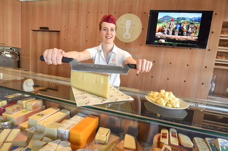 Eine Frau hinter der Verkaufstheke mit einigen Käseprodukten des Käserei-Ladens schneidet einen Käseblock an